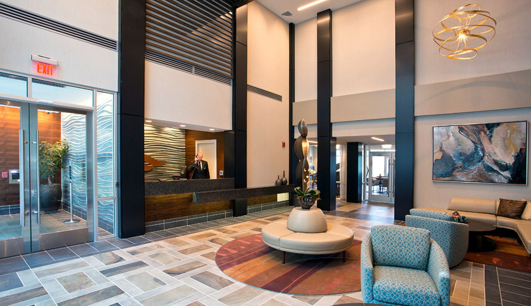 The Two-Story Lobby creates a grand entrance into the building with a slatted wood canopy and gold-leaf pendants. Custom sofas and area rugs welcome residents and visitors into the space.